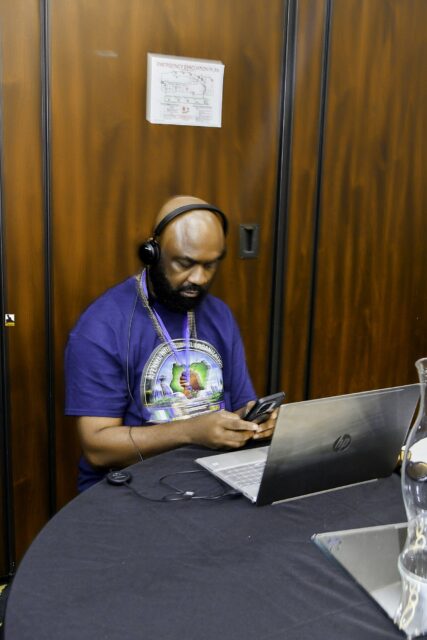 Man in a convention T-shirt seated at a laptop
