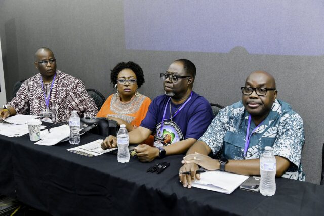 Four attendees seated behind a table with notebooks