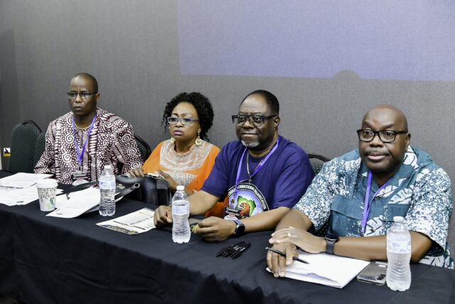 Four attendees seated behind a table with notebooks