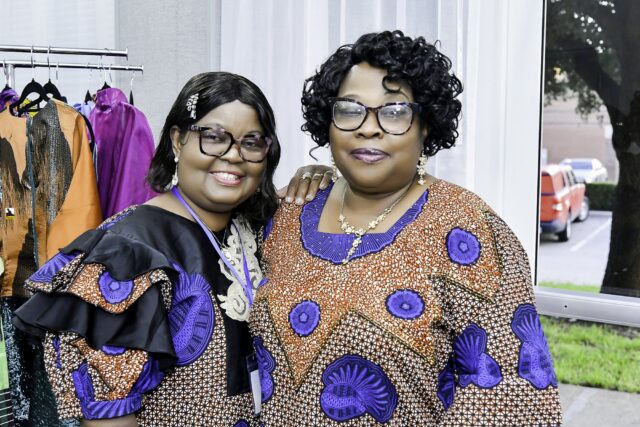 Two women in patterned blue clothing standing beside a clothing rack