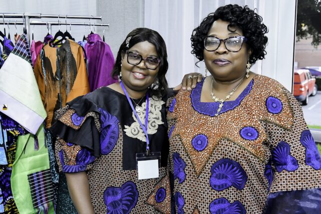 Two women in patterned blue clothing standing beside a clothing rack