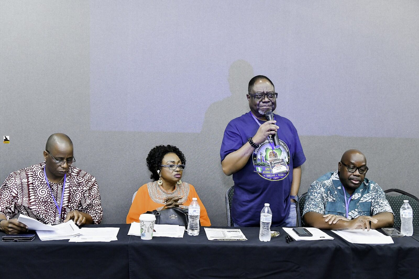 Man speaking into a microphone beside three seated attendees