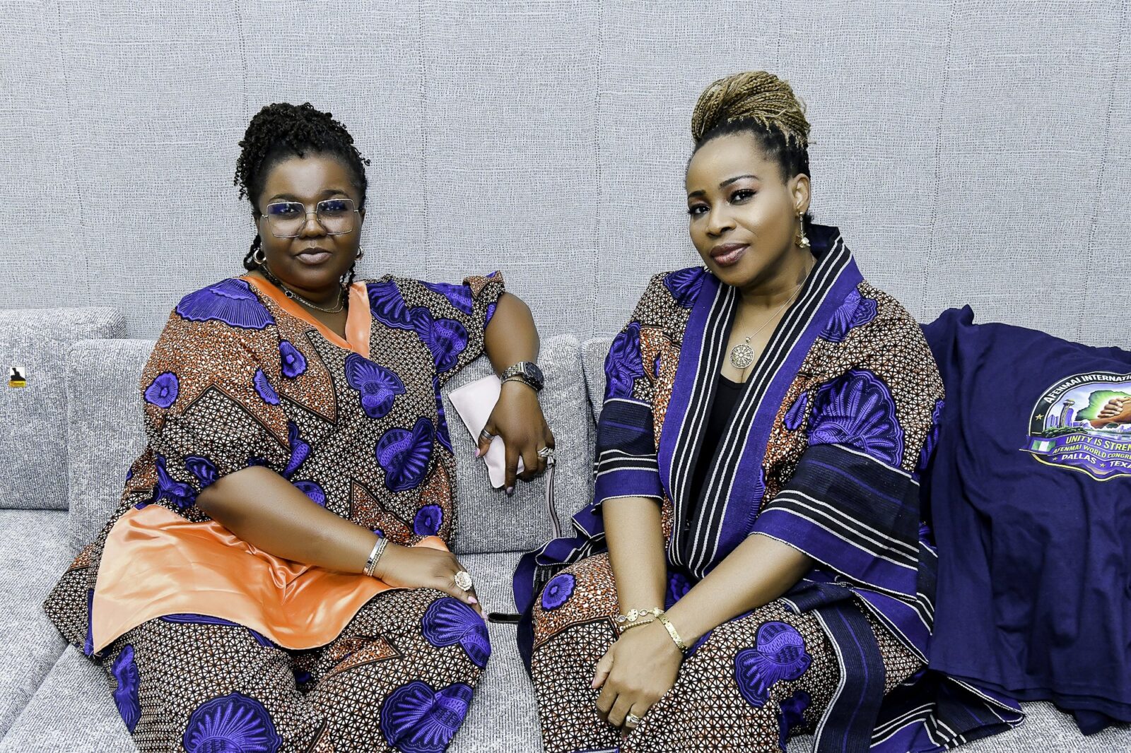 Two women in patterned clothing seated together, one wearing orange