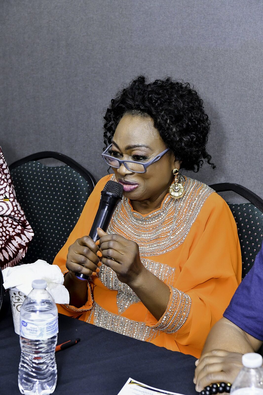 Woman in orange holding a microphone while seated