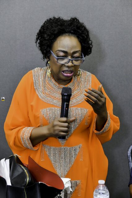 Woman in orange speaking into a microphone near the front table