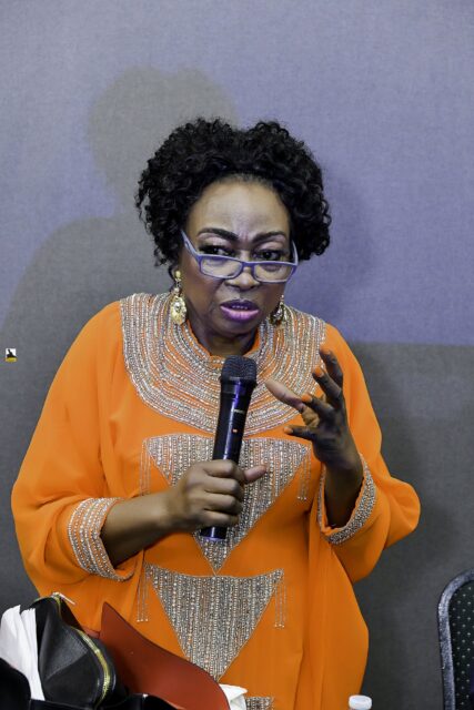 Woman in orange speaking into a microphone near the front table