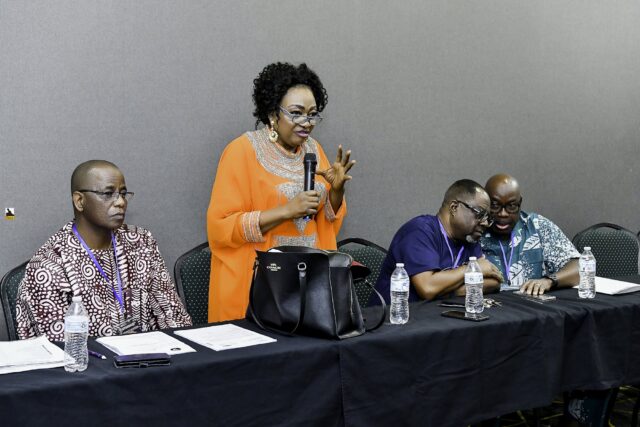 Woman in orange speaking into a microphone near the front table