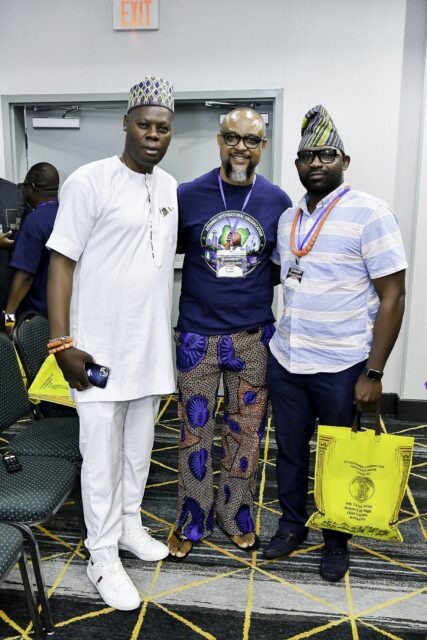 Three men standing together, two wearing caps