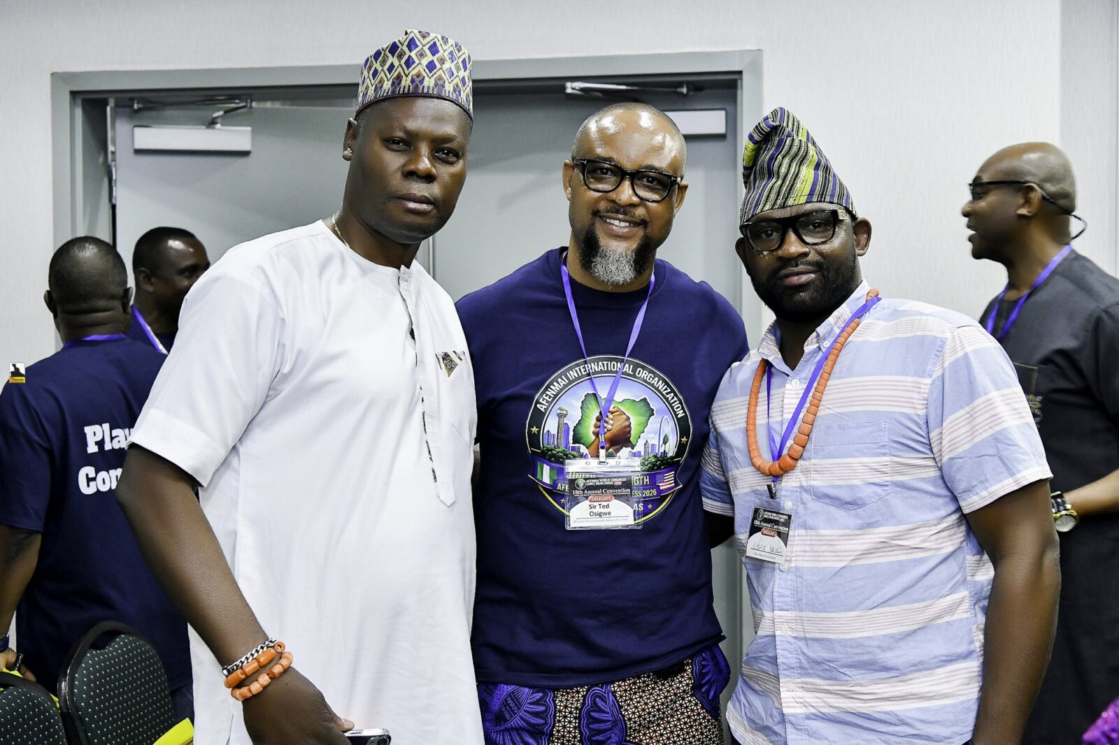 Three men standing together, two wearing caps