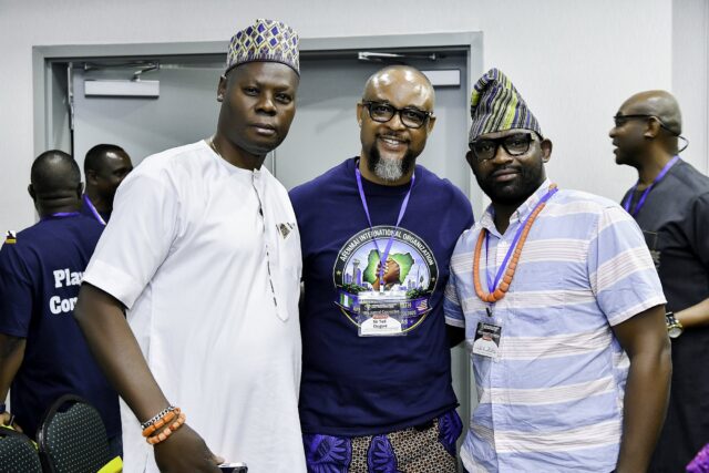 Three men standing together, two wearing caps