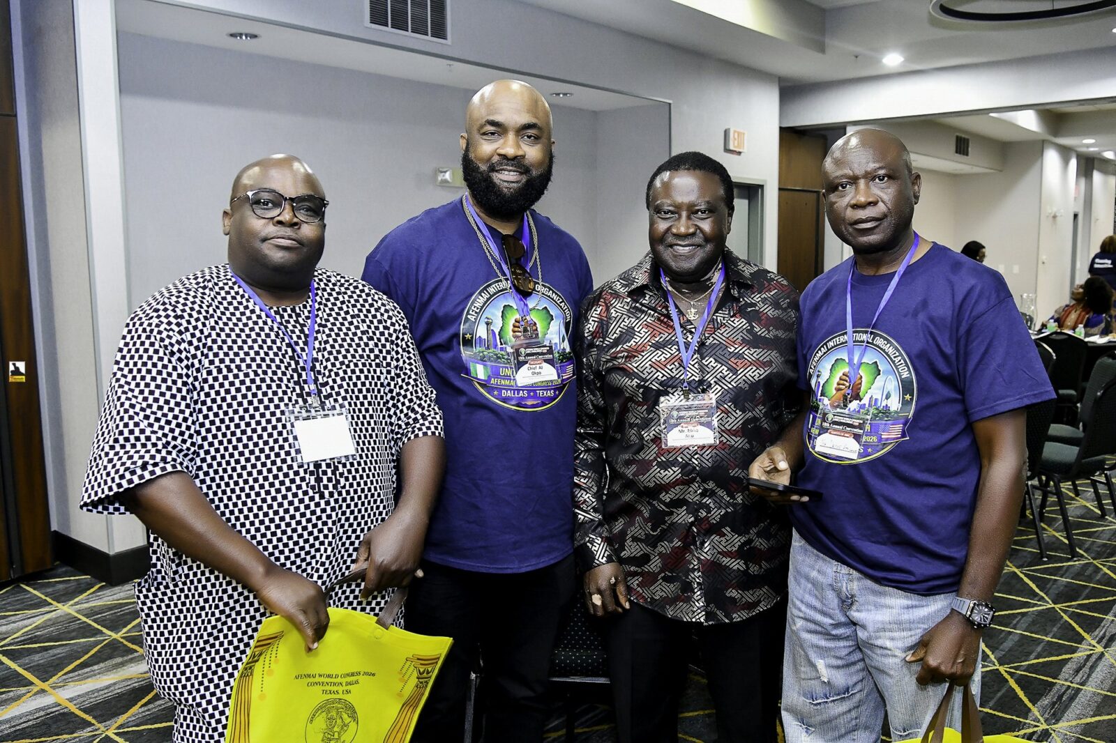 Four men in blue shirts and patterned clothing smiling together