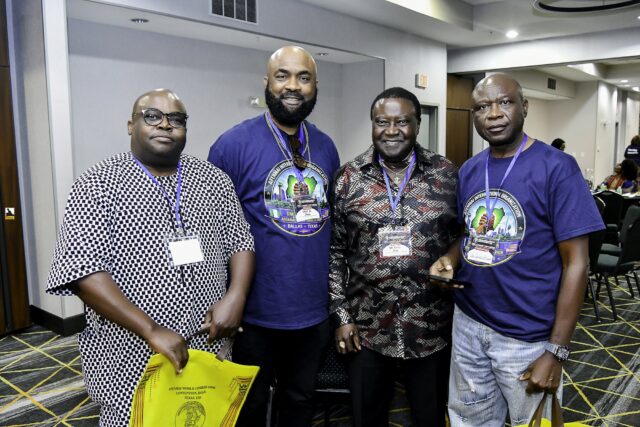Four men in blue shirts and patterned clothing smiling together