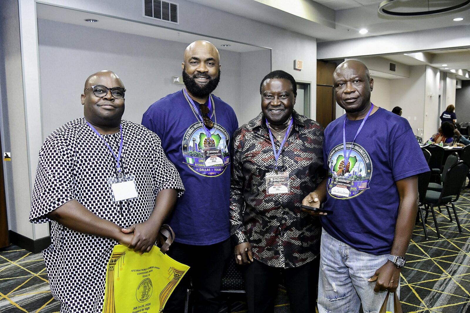 Four men in blue shirts and patterned clothing smiling together