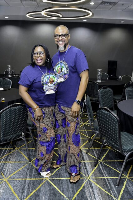 Woman in patterned clothing and man in a convention T-shirt posing together