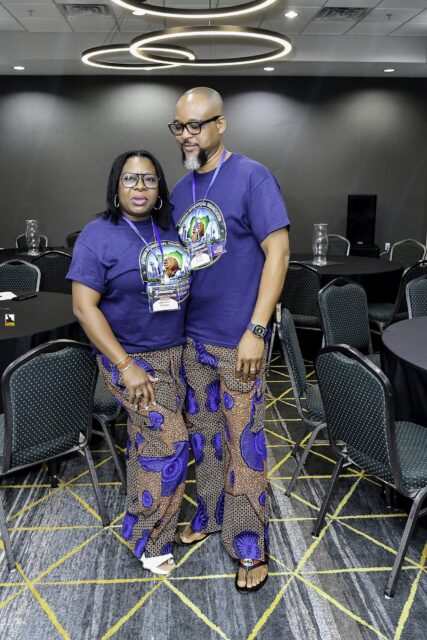 Woman in patterned clothing and man in a convention T-shirt posing together