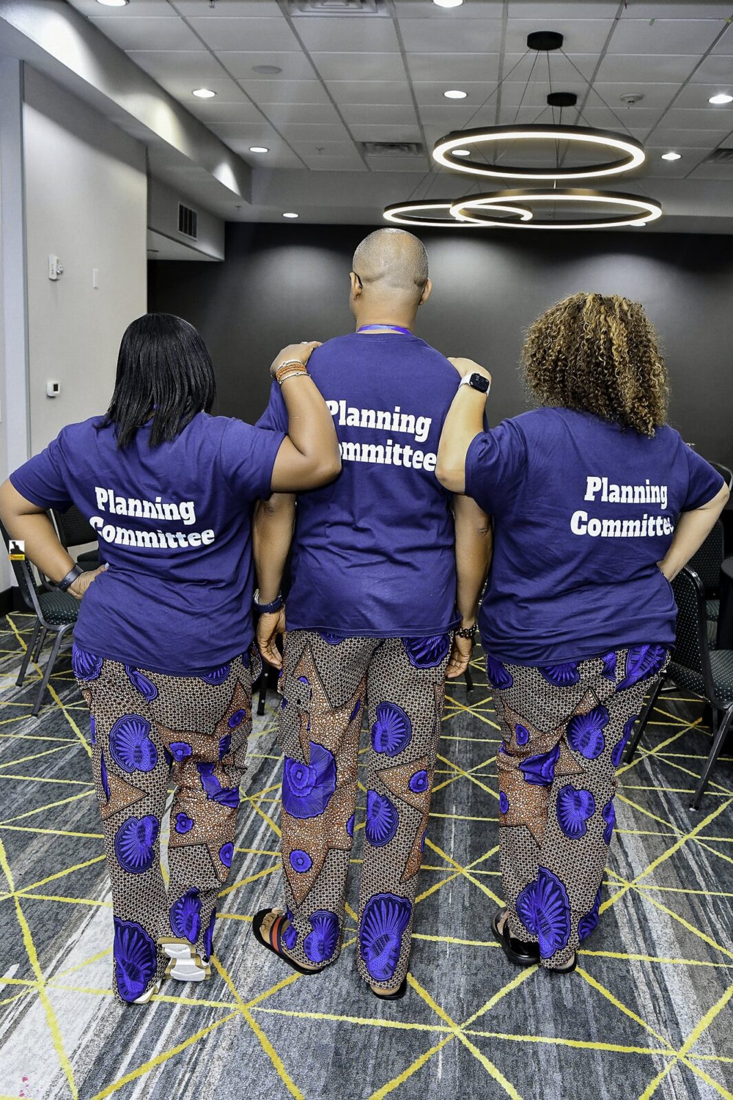 Three attendees showing the backs of their convention T-shirts