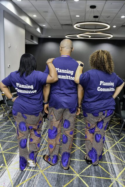 Three attendees showing the backs of their convention T-shirts