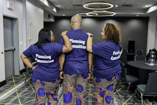 Three attendees showing the backs of their convention T-shirts