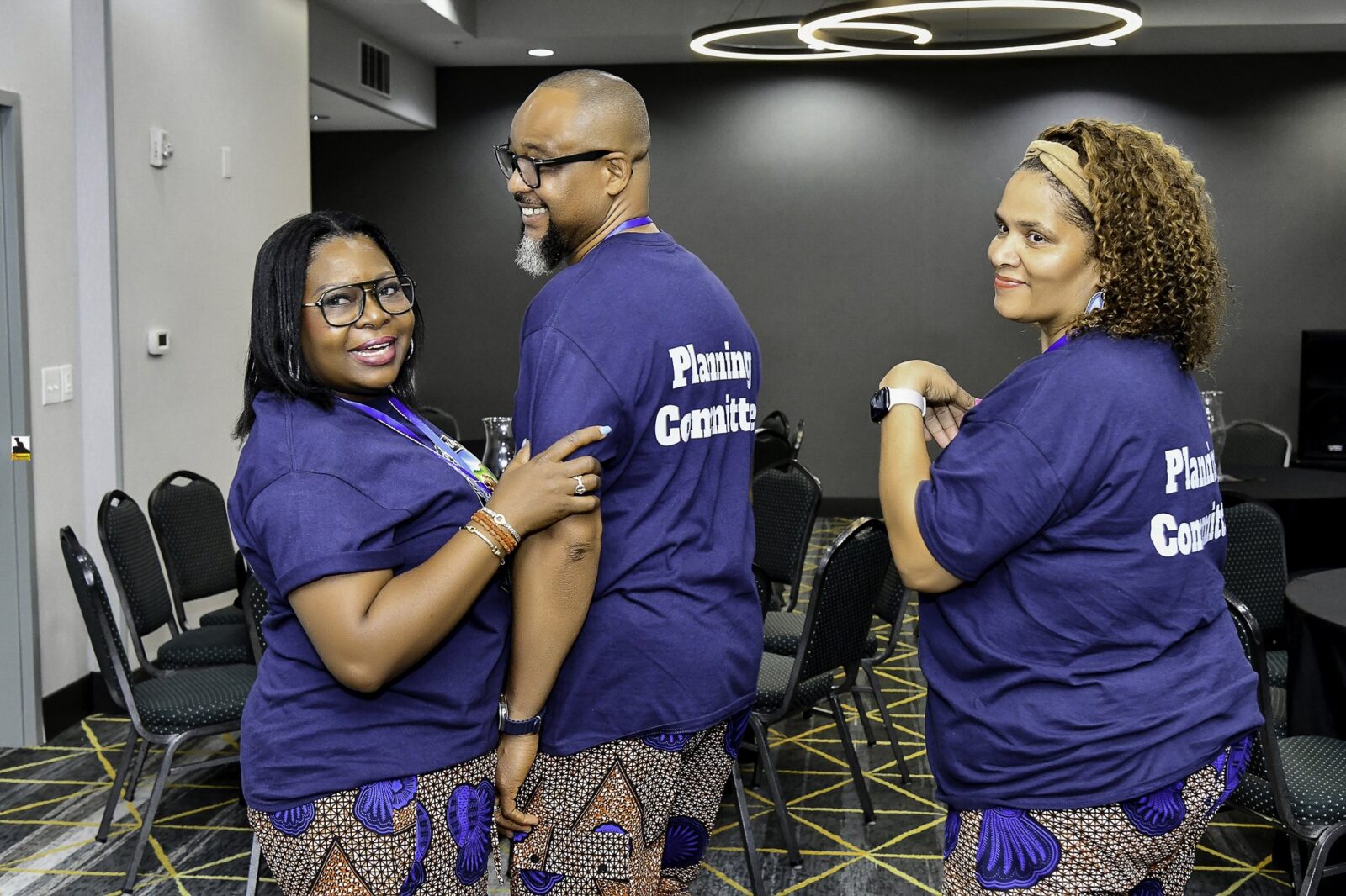 Three attendees showing the backs of their convention T-shirts