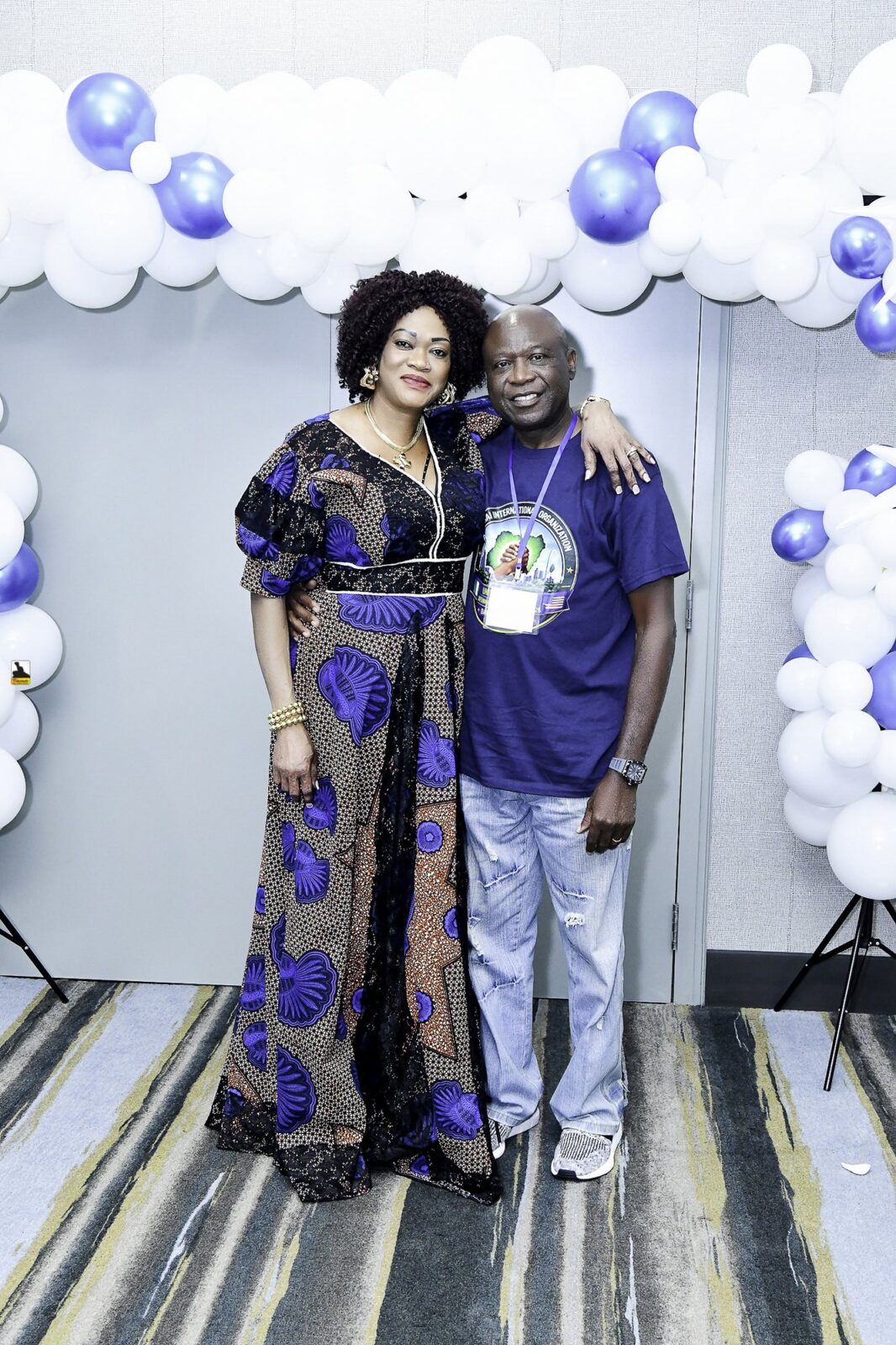Two attendees in blue clothing posing beside the balloon backdrop