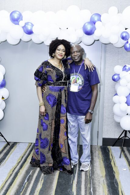 Two attendees in blue clothing posing beside the balloon backdrop