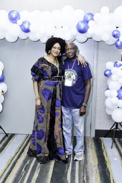 Two attendees in blue clothing posing beside the balloon backdrop