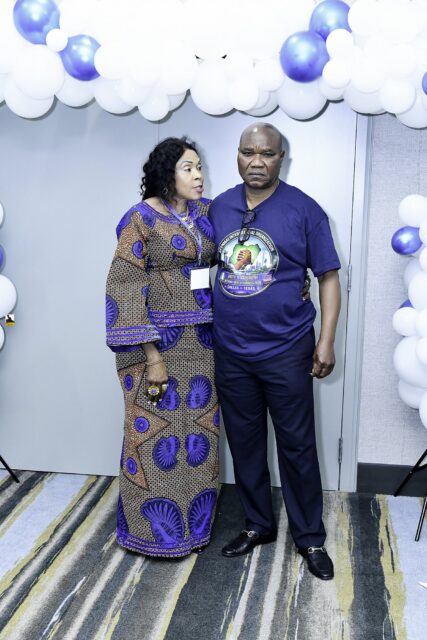 Two attendees in blue clothing posing beside the balloon backdrop