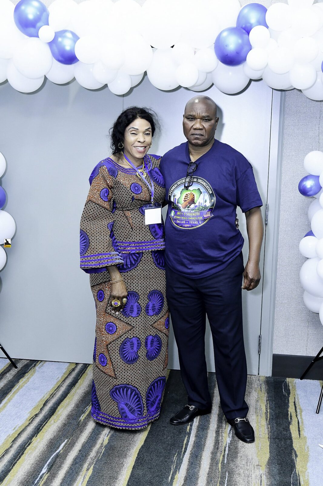 Two attendees in blue clothing posing beside the balloon backdrop