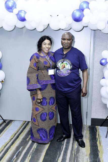 Two attendees in blue clothing posing beside the balloon backdrop