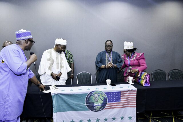 Attendees standing behind the front table beside flags