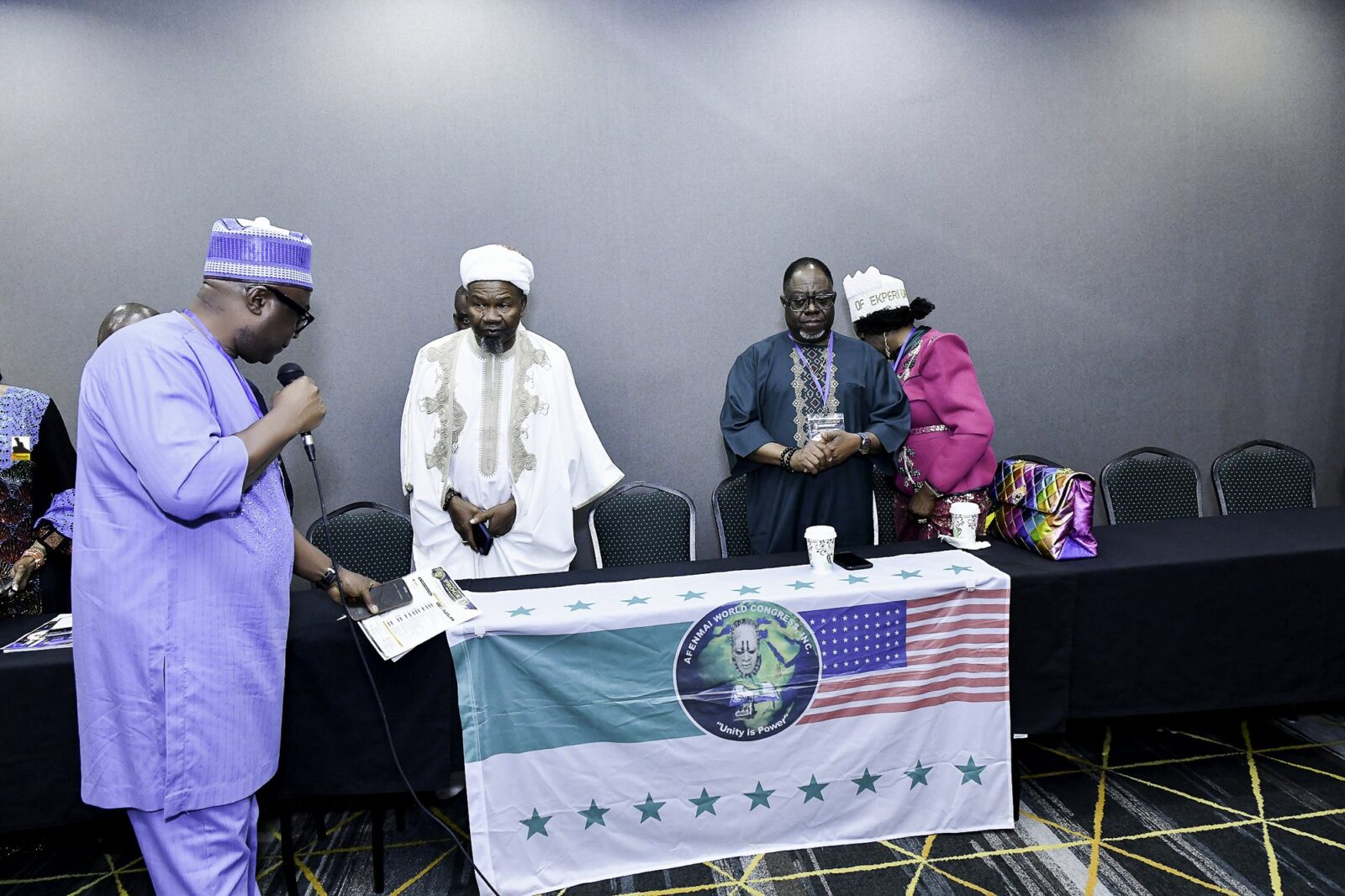 Attendees standing behind the front table beside flags