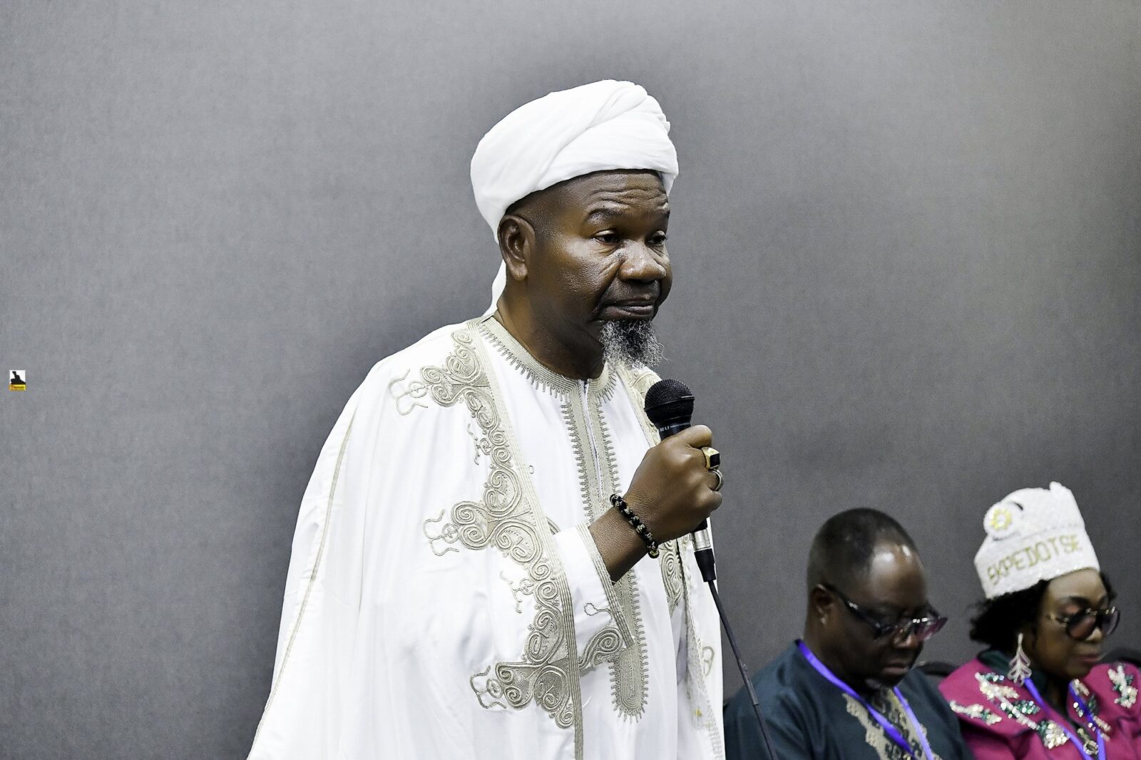 Man in white clothing speaking into a microphone