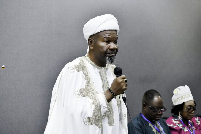 Man in white clothing speaking into a microphone