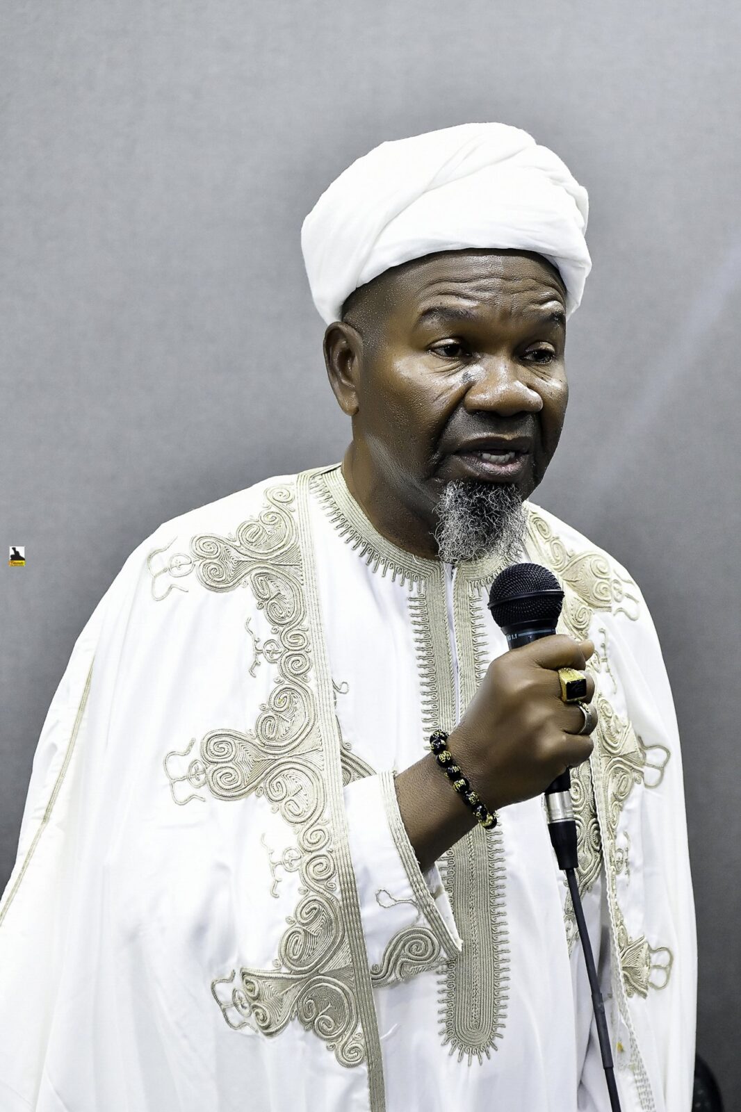 Man in white clothing speaking into a microphone