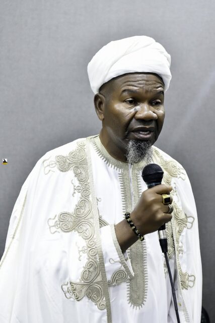 Man in white clothing speaking into a microphone