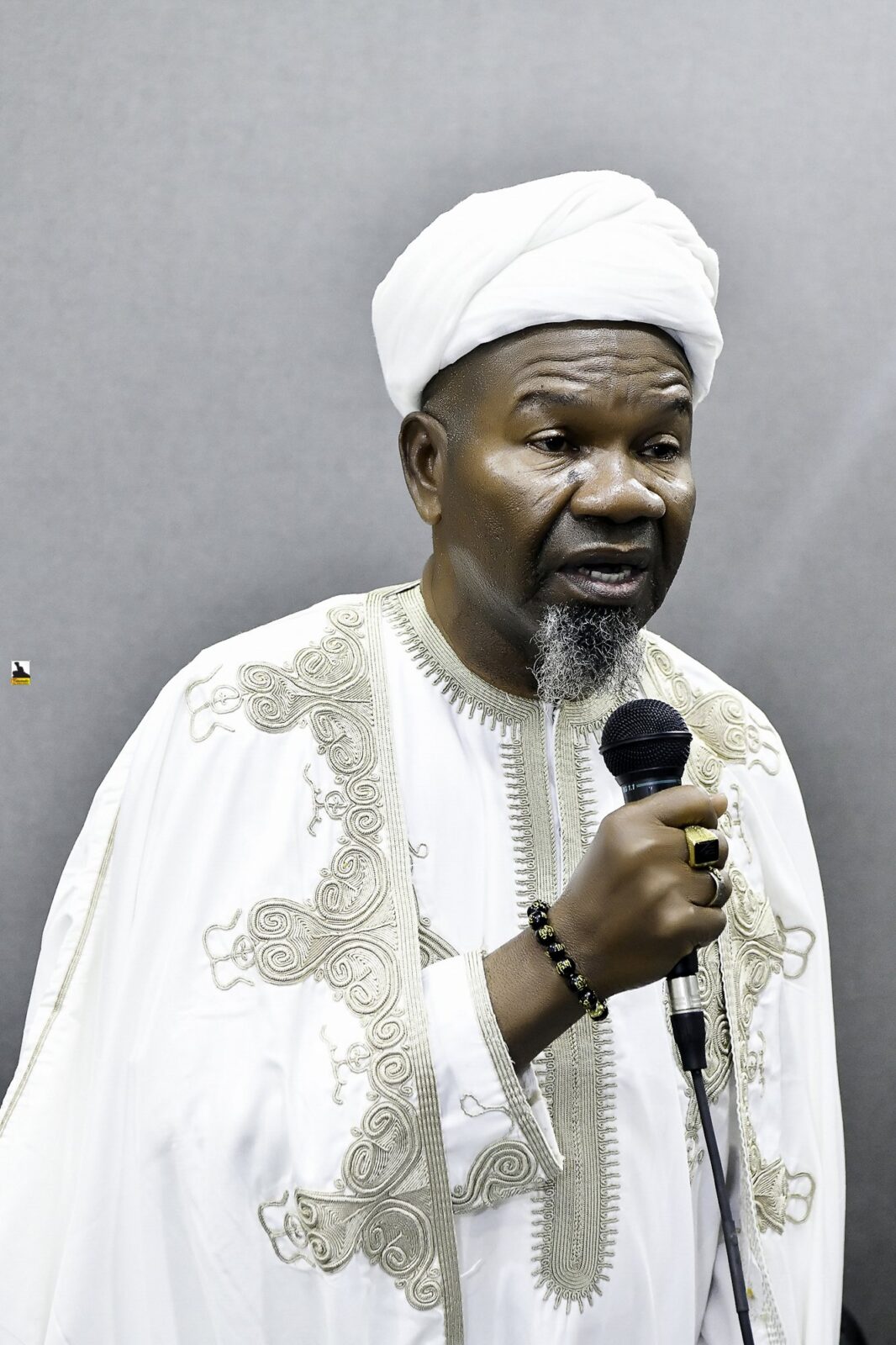 Man in white clothing speaking into a microphone
