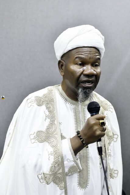 Man in white clothing speaking into a microphone