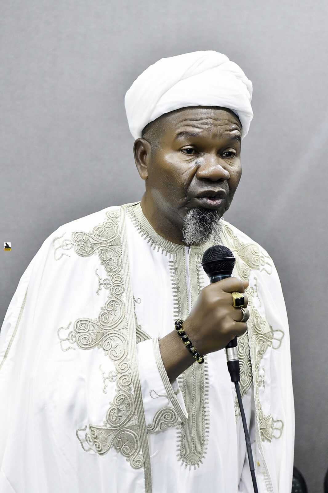 Man in white clothing speaking into a microphone