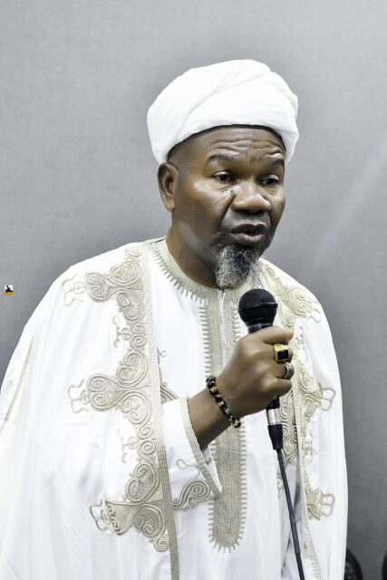 Man in white clothing speaking into a microphone