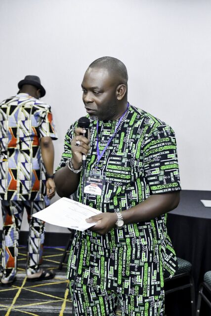 Man in a green patterned outfit reading into a microphone