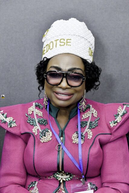 Woman in a floral jacket and white hat seated in the room