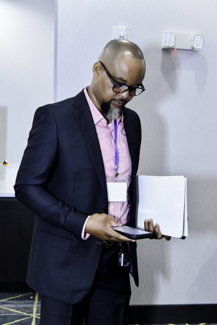 Man in a dark suit and pink shirt reading a booklet