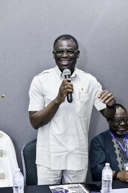 Man in a white shirt speaking into a microphone at the front table