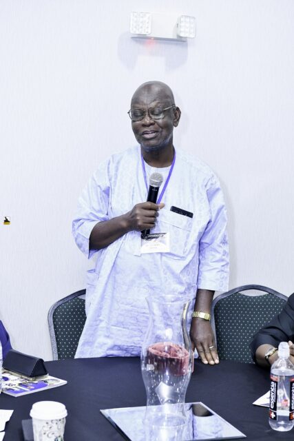 Man in white and blue clothing speaking into a microphone
