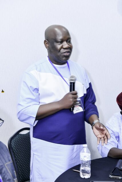 Man in white and blue clothing speaking into a microphone