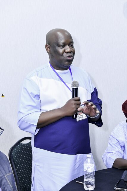 Man in white and blue clothing speaking into a microphone