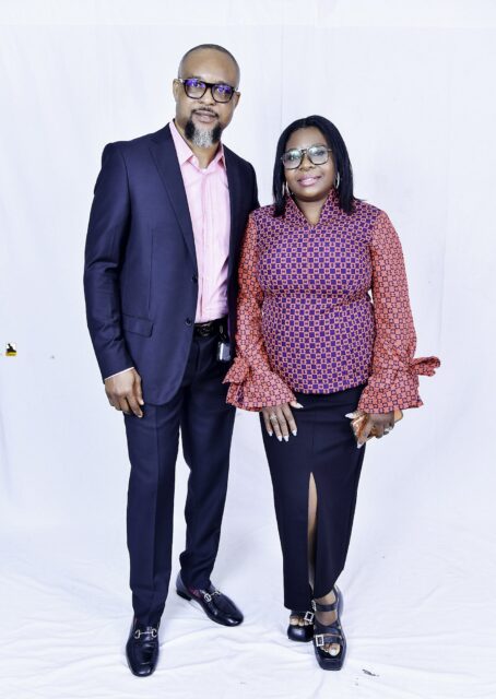 Man in a navy suit and woman in a patterned blouse posing together