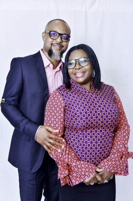 Man in a navy suit and woman in a patterned blouse posing together