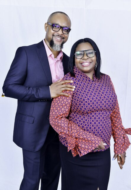 Man in a navy suit and woman in a patterned blouse posing together