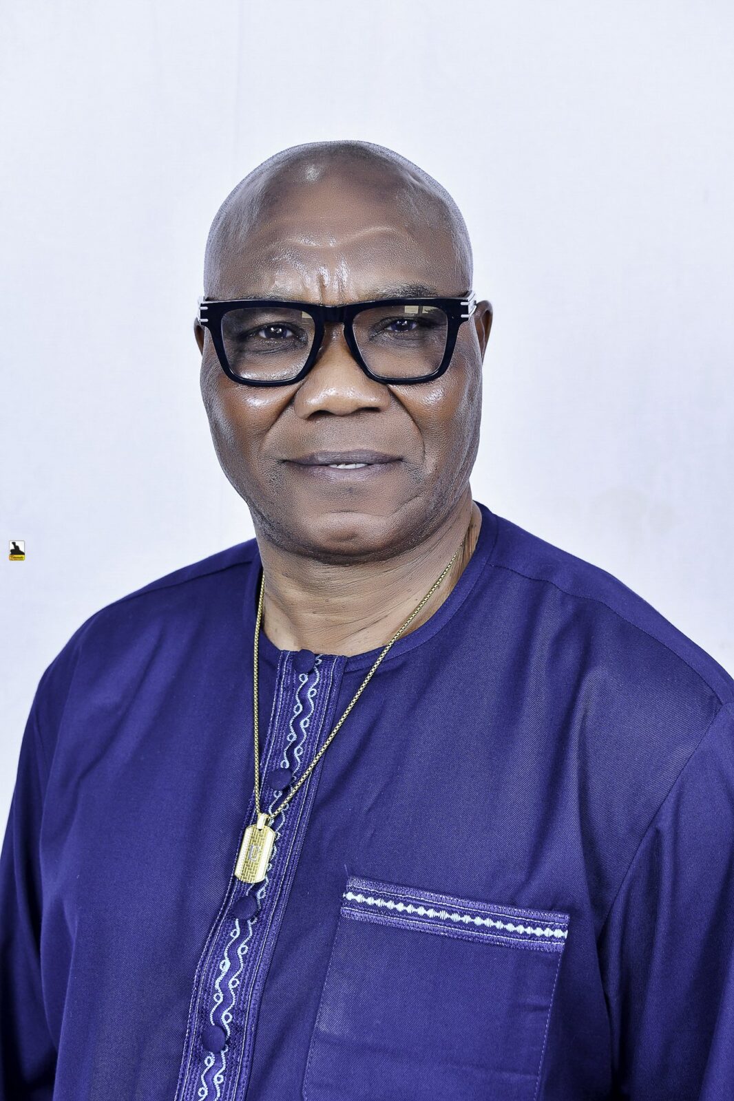 Man in dark blue clothing and glasses against a white backdrop